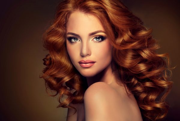 Girl with long and shiny wavy red hair . Beautiful model with curly hairstyle .